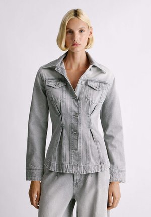 Giacca in denim grigio chiaro con una forma aderente, colletto a punta, tasche sul petto e chiusura con bottoni. Presenta dettagli di cucitura verticale.