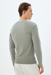 Langsleeve geribbeld shirt in gedempt groen, met een ronde hals en een getailleerd ontwerp, gecombineerd met witte broeken.