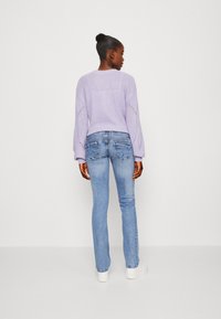 Suéter de punto lila con mangas largas y jeans ajustados azules. El conjunto presenta un diseño casual y una textura suave.