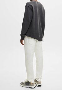 Sudadera gris, pantalones blancos hasta los tobillos. Calzado: zapatillas grises y blancas con acentos. Textura suave, corte relajado, diseño minimalista.