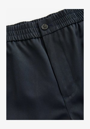 Sötétkék, könnyű anyag sima textúrával. Rugalmas derékszíjjal rendelkezik, amely gombos záródással és egy oldalsó zsebbel van ellátva.