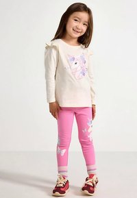 Long-sleeve cream shirt with unicorn graphic; pink leggings with butterfly patterns; sneakers with red and white accents; soft fabric.
