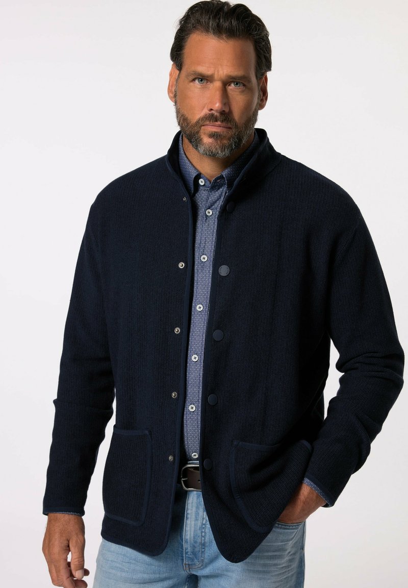 Marinblå vävd tröjjacka med ståkrage, knäppning, två framfickor, ribbad struktur och kontrasterande detaljer på ärmsluten.
