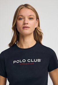 Camiseta de algodón Navy con cuello redondo, que presenta el texto blanco "POLO CLUB" y "ESTABLECIDO 2012" en rojo debajo, de manga corta.