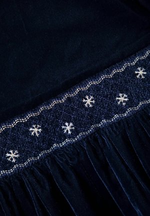 Námořnická látka s texturovaným pasem, který je zdobený bílými vyšívanými sněhovými vločkami a nařasením, vytvářejícím vrstvený vzhled.