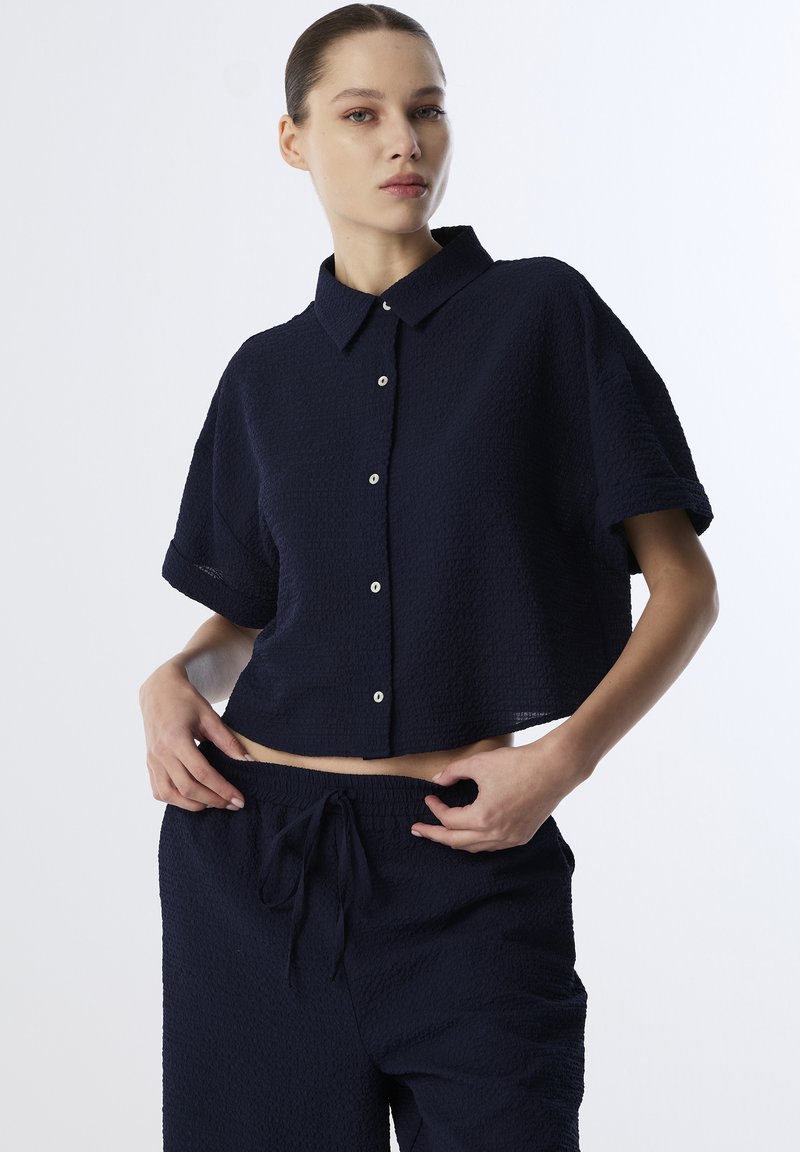 Marineblauwe, cropped shirt van een textuurstof, met knoopsluiting en korte mouwen; gecombineerd met bijpassende losse broek met een trekkoord.