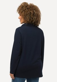 Maglia a maniche lunghe blu navy con colletto, realizzata in materiale morbido. Presenta una vestibilità comoda ed è abbinata a denim.