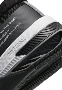 Scarpa atletica nera con tomaia texturizzata, suola intermedia bianca e suola nera dettagliata. Presenta testo stampato sulla parte superiore.