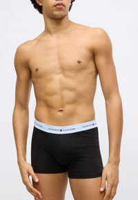 Mustad bokseripüksid helesinise vöökohaga, millel on "TOMMY HILFIGER" logo; sile kangas, keha järgiva lõike ja põlve keskpaigani ulatuva pikkusega.