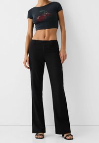 Black flared pants paired with a cropped navy t-shirt featuring red rhinestone cherries. Smooth fabric with a fitted waist and button closure.