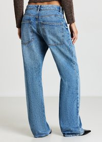 Jeans en denim bleu clair avec une coupe ample, un design à cinq poches et une taille haute. Présente des coutures visibles et un léger effilochage à l'ourlet.