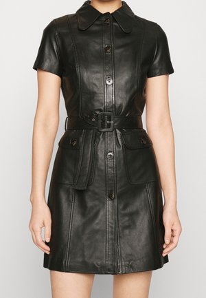 Zwarte leren korte mouwen jurk met knopen aan de voorkant, een taille met riem, een kraag en twee klepzakken, gedragen door een staand persoon.