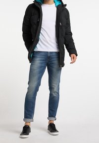 Czarna puchowa kurtka z turkusową podszewką, biała koszulka i niebieskie dżinsy. Model ma na sobie czarne trampki, stoi z luźno opuszczonymi rękami.