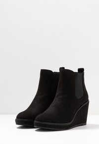 Bottines à talon compensé en suede noir avec des panneaux élastiques sur les côtés, un bout rond et des accents de couture le long de la semelle.