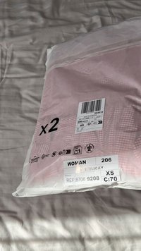 Prozirno plastično pakiranje s dva ružičasta odjevna predmeta. Oznake uključuju veličinu XS, referentni broj, barkod i upute za njegu.