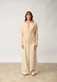 Pull beige tricoté avec un col en V et un col, associé à un pantalon large en crème à côtes. Les deux vêtements ont une texture douce, se complétant mutuellement.