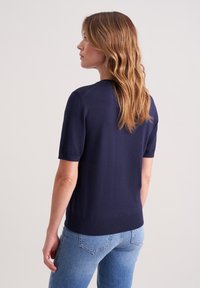 Granatowy sweter z krótkim rękawem, wykonany na drutach, z okrągłym dekoltem i prążkowanym wykończeniem. W połączeniu z jasnoniebieskimi dżinsami. Gładka, lekka tekstura.