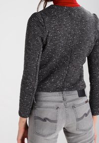 Czarny i biały sweterek w wzory z długimi rękawami, w połączeniu z szarymi dżinsami z dekoracyjnym przeszyciem na tylnych kieszeniach.