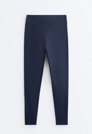 Tengerészkék, derékban magasított leggings, V alakú varrással a derékrészén, fehér háttéren kifeszítve.