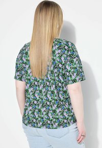 Blusa de manga corta negra con flores que presenta flores moradas y azules sobre un fondo verde, hecha de una tela ligera, de corte relajado.