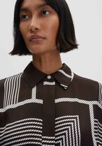 Blusa marrone con un motivo geometrico di corda bianca, colletto classico, chiusura con bottoni e texture liscia.