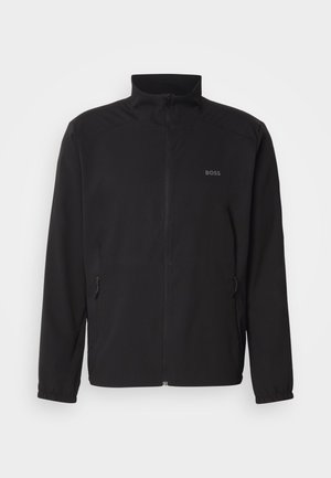 Schwarze Jacke mit Stehkragen, frontalem Reißverschluss und zwei Seitentaschen. Besitzt ein dezentes Logo auf der linken Brust und elastische Bündchen.