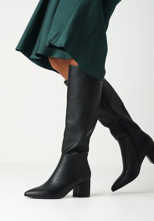 Bottes noires en cuir, hauteur genou, avec un bout pointu, un talon épais et une fermeture éclair sur le côté ; texture lisse avec des détails de design minimalistes.