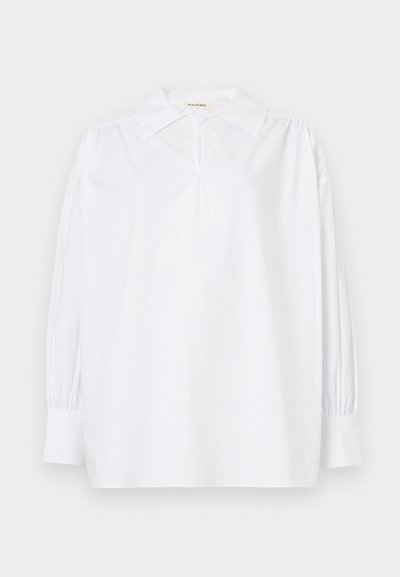 Valge pika varrukaga pluus terava krae, kogutud õlgade, nööpidega varrukasääre ja väikese nööbiga kaeluses.