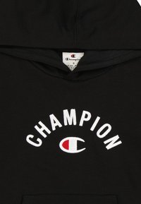 Felpa nera con cappuccio ampio, con testo ricamato bianco "CHAMPION" e logo. Tessuto morbido con tasca frontale, design casual.