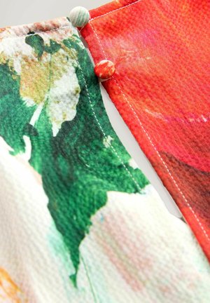 Stof med levende blomstertryk i grøn, rød og pink; har dekorative knapper i matchende farver; syede kanter.