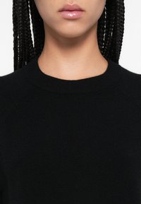 Μαύρο πλεκτό πουλόβερ με ριμπ λαιμόκοψη και μανίκια ράγκλαν. Το ύφασμα φαίνεται μαλακό με ομαλή υφή. Μινιμαλιστικός σχεδιασμός.