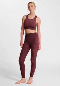 Bordeauxrode sports-bh met ribstructuur en high-waisted leggings, voorzien van verticale streepdetails en een aansluitend ontwerp. Zacht, rekbaar materiaal.
