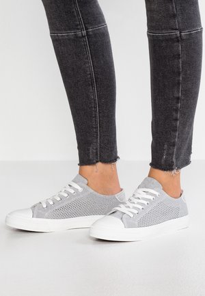 Šedé síťované tenisky s bílými gumovými špičkami a tkaničkami. Mají strukturovaný svršek a nízký profil. N Carry with black, frayed jeans.