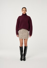 Burgunderfarbener Strickpullover mit hohem Kragen, kombiniert mit einem strukturierten beigen Minirock, der mit Verzierungen geschmückt ist, und knielangen schwarzen Lederstiefeln.