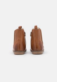 Une paire de bottines en cuir marron avec des détails de couture et de petites languettes, présentées de dos sur un fond blanc.