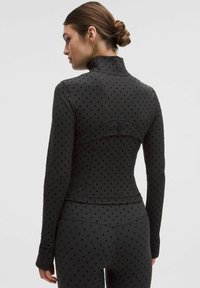 Top negro de manga larga con cuello alto, que presenta una textura de lunares, un diseño ajustado y una costura trasera contorneada para un ajuste personalizado.