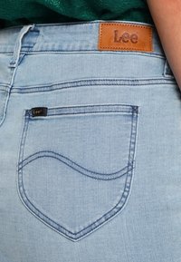 Ljusblå denimjeans med en distinkt bakficka med en böjd söm och en brun läderlapp märkt "Lee."
