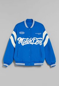 Niebieska kurtka typu varsity wykonana z teksturowanej tkaniny, z białymi paskami na rękawach i kołnierzu, z nadrukiem "Match Day" oraz innymi wzorami tekstowymi.