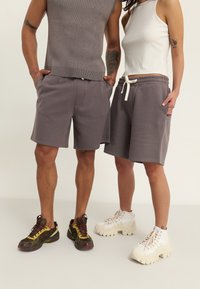 Gray cotton shorts with elastic waistband and drawstring, paired with ribbed sleeveless tops. Model footwear includes multicolored and white sneakers.