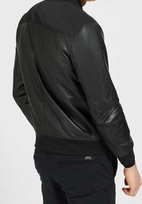 Bomber jacket in pelle nera con colletto e polsini a costine, caratterizzato da una texture liscia e dettagli di cucitura sottili sul retro.