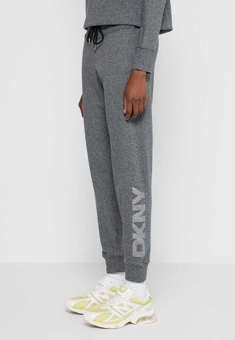 Szare dresowe spodnie z polaru z elastycznym pasem na sznurek, bocznymi kieszeniami i białym napisem "DKNY" na lewej nogawce. Noszone z białymi i żółtymi trampkami.
