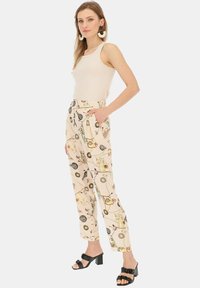 Jasnobeżowe spodnie z kolorowym wzorem przedstawiającym nożyczki i motywy szycia. Wykonane z miękkiego materiału; posiadają boczne kieszenie oraz luźny krój.