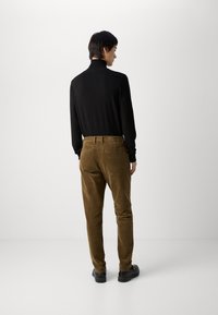 Svart åtsittande långärmad topp med hög krage, olivgröna kordbyxor och svarta skor. Slätt tyg och texturerad kord, åtsittande design med bakfickor.