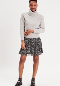 Suéter gris de cuello alto y grueso combinado con una falda negra de patrón floral y acampanada. Texturas suaves y botas negras hasta el tobillo completan el look.