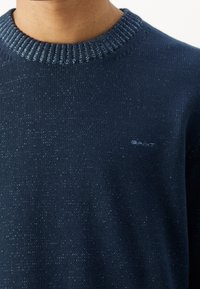 Marineblauer Pullover mit geripptem Halsauschnitt, subtiler Textur und einem kleinen Logo in einer helleren Farbe auf der Brust.