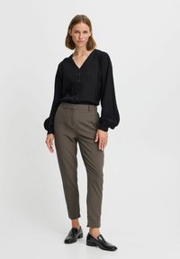 Black ribbed blouse with a V-neckline and button detailing, paired with tapered olive green trousers and shiny black slip-on shoes.