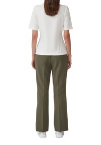 T-shirt blanc à manches courtes associé à un pantalon vert olive, à coupe droite, porté avec des baskets blanches.