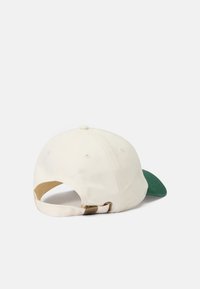 Baseball cap with a cream crown and a green brim. Features a breathable fabric and an adjustable strap with metal hardware on the back.