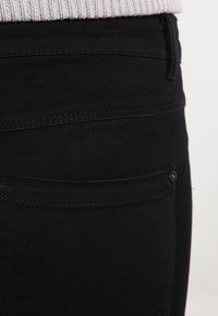 Primer plano de unos vaqueros de mezclilla negra, con un diseño limpio, textura suave y un bolsillo trasero minimalista con un pequeño detalle de botón.