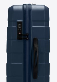 Námorní modrý tvrdý kufr s texturovaným povrchem, s kombinovaným zámkem, tvarovanou rukojetí a zesílenými rohy pro zvýšenou odolnost.